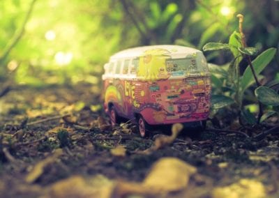 A toy hippie van in the dirt with plants around